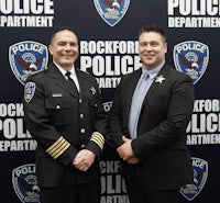 two men in uniform standing in front of a rockford police department banner